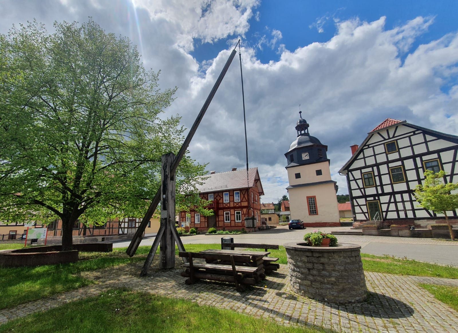 Dorfplatz mit Brunnen und Pension im Hintergrund